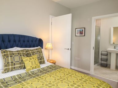 A bedroom with a bed with yellow and gray plaid bedding a nightstand with a lamp and an open door leading to a bathroom at The Pottery in Newport Pembrokeshire