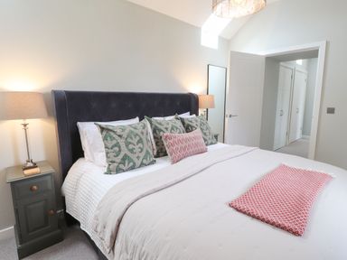 A bedroom with a bed with multiple pillows bedside tables with lamps and an open door at The Pottery in Newport Pembrokeshire