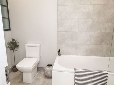A bathroom with a toilet a bathtub a striped towel a green plant and a decorative pot at The Pottery in Newport Pembrokeshire