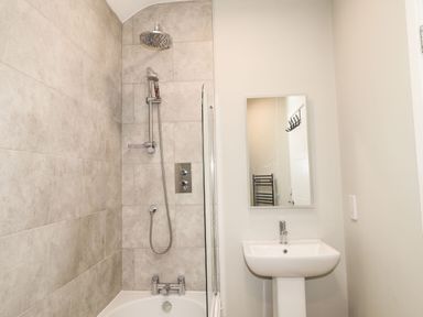 A bathroom with a bathtub shower combination and a sink with a mirror at The Pottery in Newport Pembrokeshire