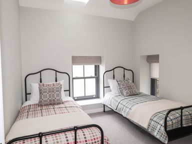 A bedroom with two single beds and patterned bedding by windows at The Pottery in Newport Pembrokeshire