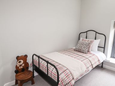 A single bed with patterned bedding and pillows next to a wooden teddy bear chair in a bedroom at The Pottery in Newport Pembrokeshire