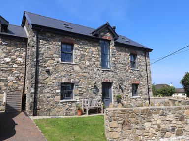 The front view of a stone house with grey windows a bench and a low stone wall at The Pottery in Newport Pembrokeshire