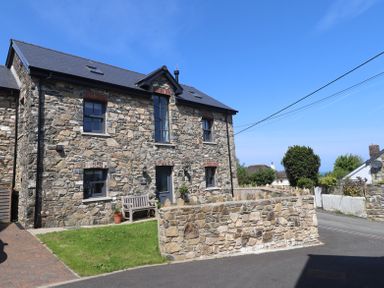 A stone house with a bench and a low stone wall along the street at The Pottery in Newport Pembrokeshire
