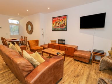 A living room with leather sofa and chairs a wooden dining table and TV on the wall at Bronwen House in Llanbedr