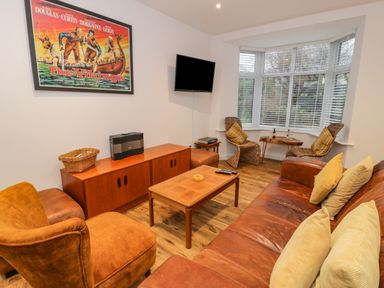 A living room with brown leather sofa and armchair wooden coffee table and two wicker chairs near a bay window at Bronwen House in Llanbedr