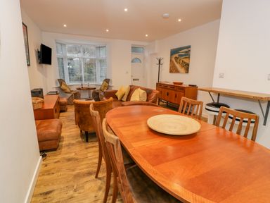 A dining and living room with wooden table and chairs leather sofas and a painting on the wall at Bronwen House in Llanbedr