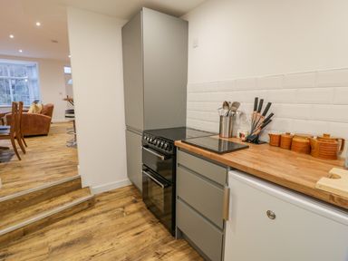 A kitchen area with grey cabinets a stove countertop with utensils and ceramic containers and a view into a dining and living area at Bronwen House in Llanbedr