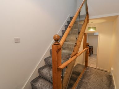A carpeted staircase with wooden handrails and glass panels next to a hallway with a light fixture and a doorway at Bronwen House in Llanbedr