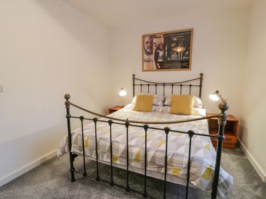 A bedroom with a metal bed frame yellow pillows bedside tables with lamps and a movie poster on the wall at Bronwen House in Llanbedr