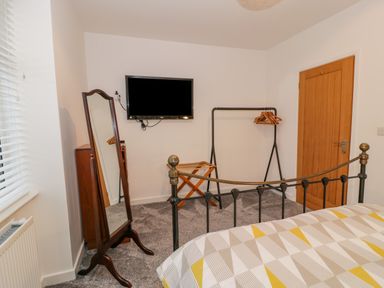 A bedroom with a bed metal frame a freestanding mirror a wall-mounted television a wooden door and a clothes rack with hangers at Bronwen House in Llanbedr