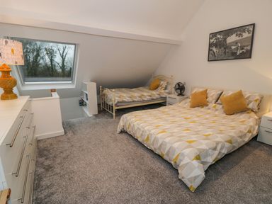 A bedroom with two beds a dresser a lamp and a window at Bronwen House in Llanbedr