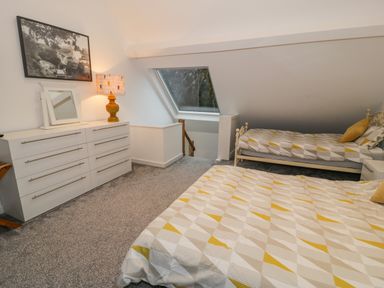 A bedroom with a large bed and a single bed a white dresser with a lamp and a framed picture on the wall at Bronwen House in Llanbedr