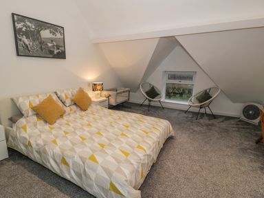 A bedroom with a bed a nightstand two chairs and a small window at Bronwen House in Llanbedr