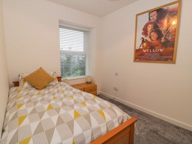 A small bedroom with a single bed covered in geometric patterned bedding a window with blinds two wooden bedside tables and a framed willow movie poster on the wall at Bronwen House in Llanbedr