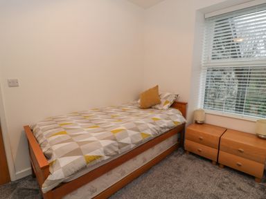 A bedroom with a single bed and patterned bedding next to two wooden nightstands with lamps by a window at Bronwen House in Llanbedr
