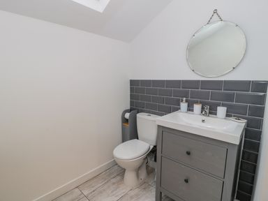 A bathroom with a toilet sink vanity with mirror and grey tiled backsplash at Bronwen House in Llanbedr
