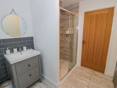 A bathroom with a sink and round mirror next to a glass shower enclosure and a wooden door at Bronwen House in Llanbedr