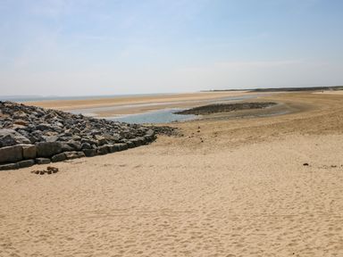 A sandy beach with a pile of rocks on the left and the ocean in the background at Ty Crydd in Llansaint near Kidwelly