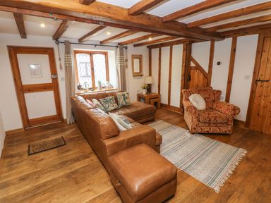 A living room with a brown leather sectional sofa red patterned armchair wooden beams and floor at Ty Crydd Llansaint near Kidwelly