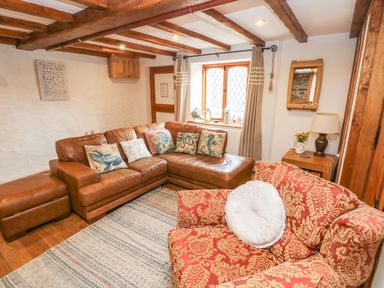 A living room with brown leather sectional sofa and red patterned armchair at Ty Crydd in Llansaint near Kidwelly
