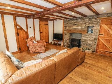 A living room with wooden beams exposed walls stone fireplace with stove leather sofa and armchair at Ty Crydd in Llansaint near Kidwelly