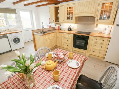 A kitchen with cream cabinets a dining table set with yellow teacups and a vase of white tulips at Ty Crydd in Llansaint near Kidwelly