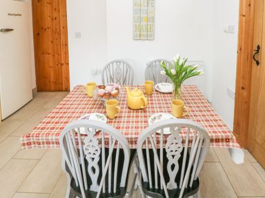 A dining table with a red checkered tablecloth set with yellow mugs plates a yellow teapot cupcakes and white flowers in a vase in a kitchen at Ty Crydd Llansaint near Kidwelly