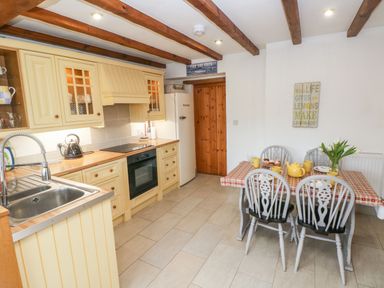 A kitchen with cream cabinets wooden beams a dining table and chairs at Ty Crydd in Llansaint near Kidwelly