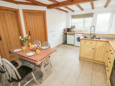 A kitchen with a dining table set for four and appliances along the wall at Ty Crydd in Llansaint near Kidwelly
