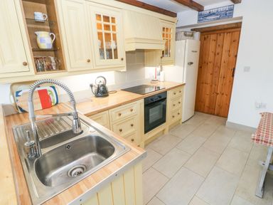 A kitchen with a wooden countertop a stainless steel sink a black kettle a refrigerator and wooden cabinets at Ty Crydd Llansaint near Kidwelly
