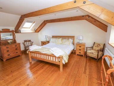 A bedroom with a wooden bed a dresser and chairs under wooden beams at Ty Crydd in Llansaint near Kidwelly