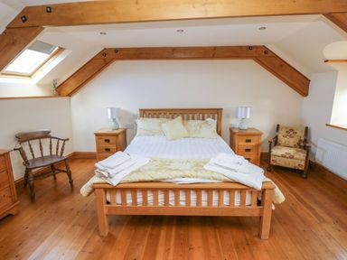 A bedroom with a wooden bed and side tables with lamps under a slanted ceiling with wooden beams at Ty Crydd in Llansaint near Kidwelly
