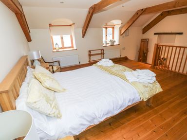 A bedroom with a wooden bed white and yellow bedding wooden floors and ceiling beams at Ty Crydd in Llansaint near Kidwelly