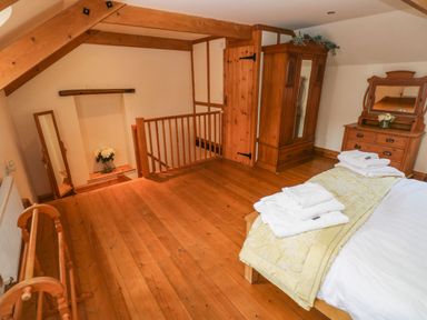 A bedroom with wooden floor beams wardrobe dresser bed and towels at Ty Crydd in Llansaint near Kidwelly