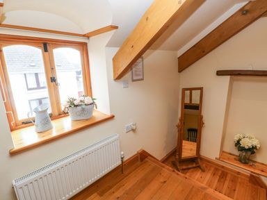 A stairway landing with a wooden floor a window with flower pots a standing mirror and wooden beams at Ty Crydd in Llansaint near Kidwelly