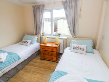 A bedroom with two single beds a wooden drawer unit between them and a window with curtains at Ty Crydd in Llansaint near Kidwelly