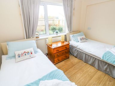 A bedroom with two single beds separated by a wooden nightstand with lamps and a window at Ty Crydd in Llansaint near Kidwelly