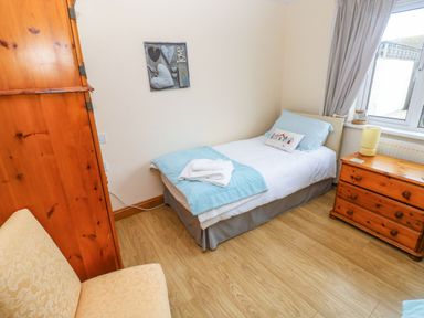 A bedroom with a single bed a wooden wardrobe a chest of drawers a chair and a window at Ty Crydd in Llansaint near Kidwelly