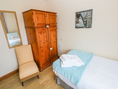 A bedroom with a wooden wardrobe a beige chair a bed with folded towels and a blue blanket at Ty Crydd in Llansaint near Kidwelly