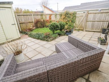 A fenced backyard with a garden shed wicker sofa and small plants at Ty Crydd in Llansaint near Kidwelly