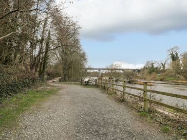 A gravel pathway along a river with a wooden fence and trees and a bridge in the background at Belle Vue in Hay on Wye Herefordshire