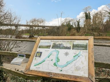 A wooden framed map sign showing Welcome to Hay-on-Wye near a river with trees and a bridge in the background at Belle Vue in Hay on Wye Herefordshire
