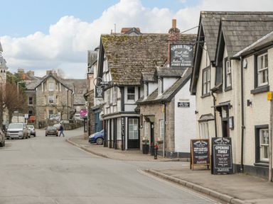 A street with old stone and white buildings including a pub with signs and parked cars in a town