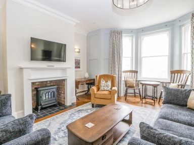 A living room with a fireplace a wall mounted TV a brown armchair wooden chairs and a coffee table at Belle Vue in Hay on Wye Herefordshire