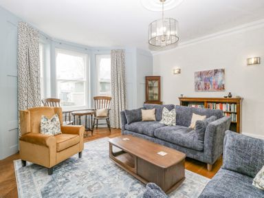 A living room with a brown armchair gray sofas wooden coffee table and bay windows at Belle Vue in Hay on Wye Herefordshire