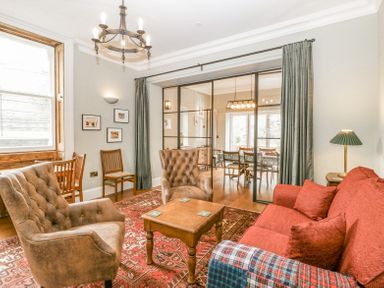 A living room with two armchairs a red sofa and a wooden coffee table facing a dining room behind glass doors at Belle Vue in Hay on Wye Herefordshire