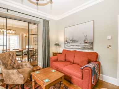 A living room with an orange sofa brown armchair wooden table and painting on the wall at Belle Vue in Hay on Wye Herefordshire