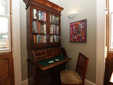 A wooden writing desk with books inside a glass cabinet and a chair next to a wall with abstract art at Belle Vue in Hay on Wye Herefordshire