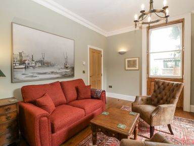 A living room with a red sofa a brown armchair a wooden coffee table a large window and a painting of boats at Belle Vue in Hay on Wye Herefordshire